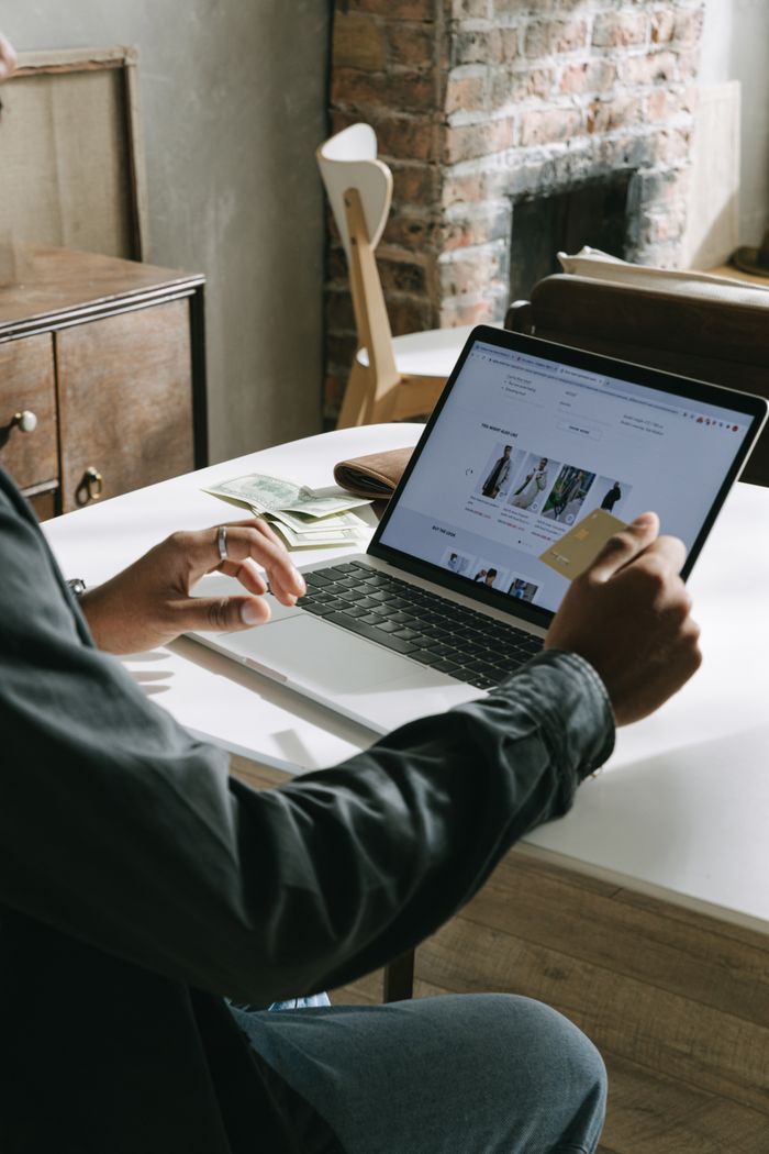 An adult uses a credit card for online shopping on a laptop indoors.